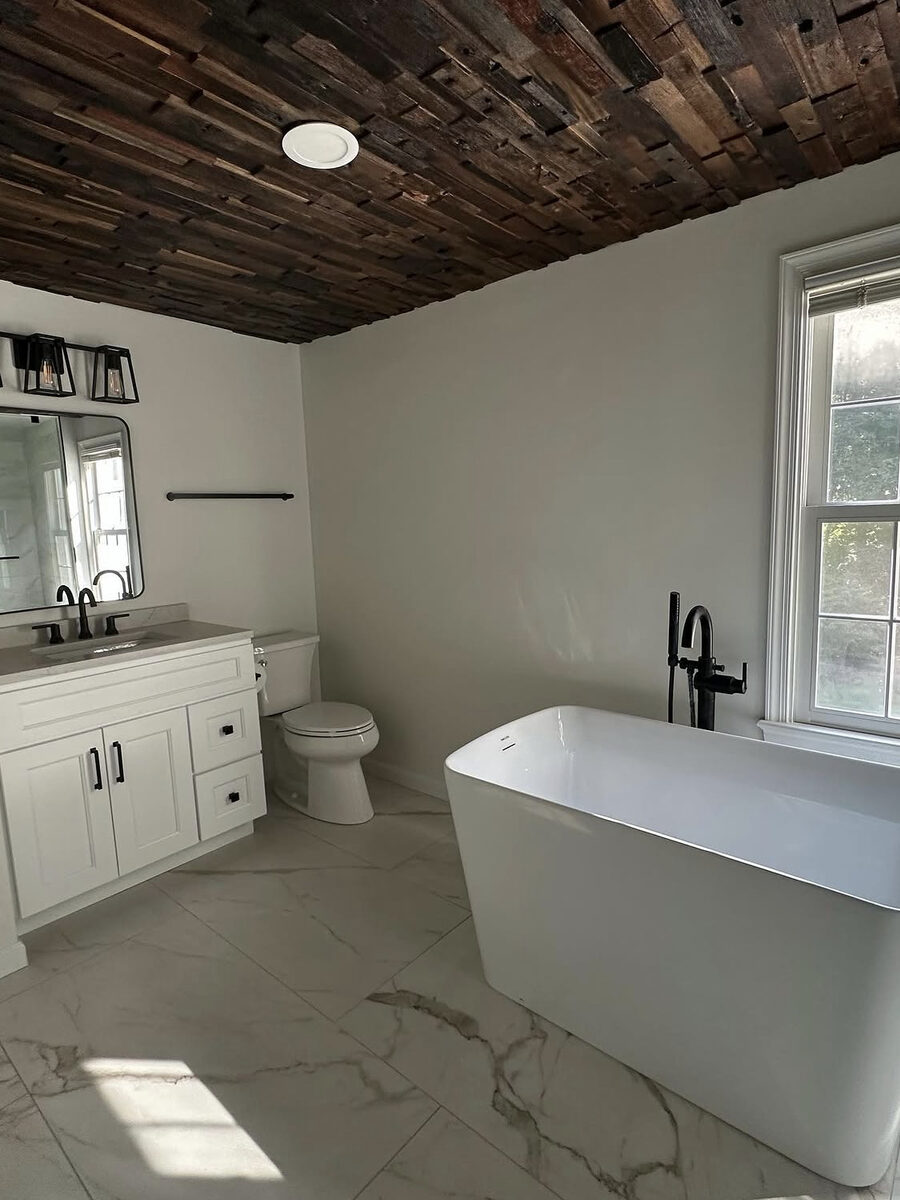 Bathroom remodel with freestanding tub, marble-look tile, and reclaimed wood plank ceiling