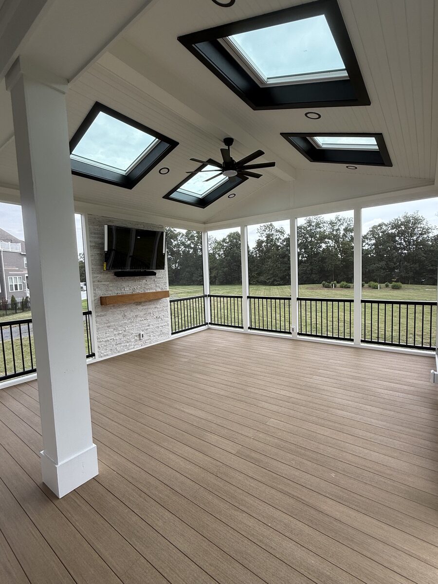 Covered porch outdoor living room with stone fireplace, TV, and cathedral ceiling